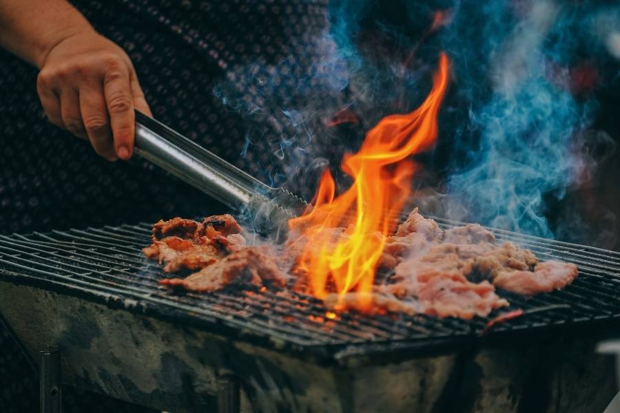 Viande grillée sur un barbecue en pierre, entourée de flammes et de fumée, pour un repas délicieux.