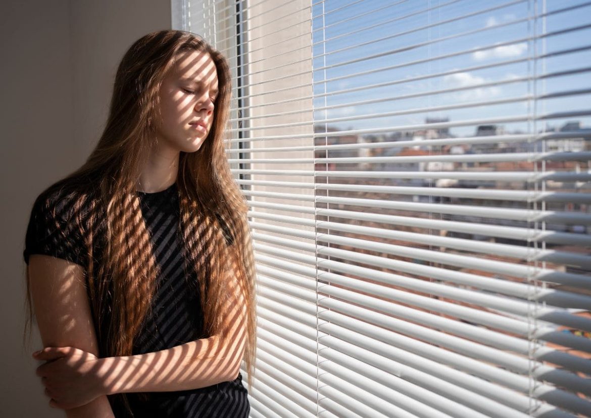 Jeune femme devant un volet roulant, le visage marqué par les ombres des lames.