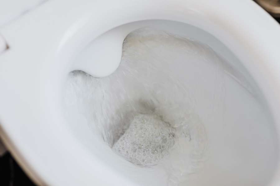 Chasse d'eau en action dans une cuvette de toilettes blanche avec de l'eau tourbillonnante et mousseuse
