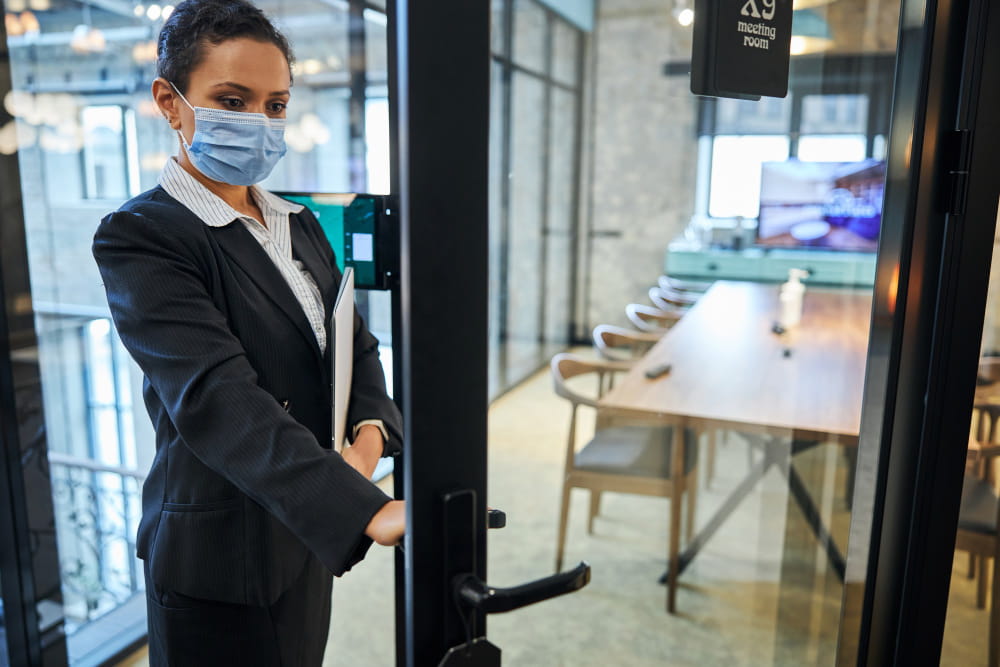 Une professionnelle portant un masque de protection ouvre la porte d'une salle de réunion équipée d'un système de contrôle d'accès en entreprise