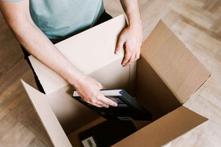 Un employé range soigneusement des livres et dossiers dans un carton durant un déménagement de bureaux.