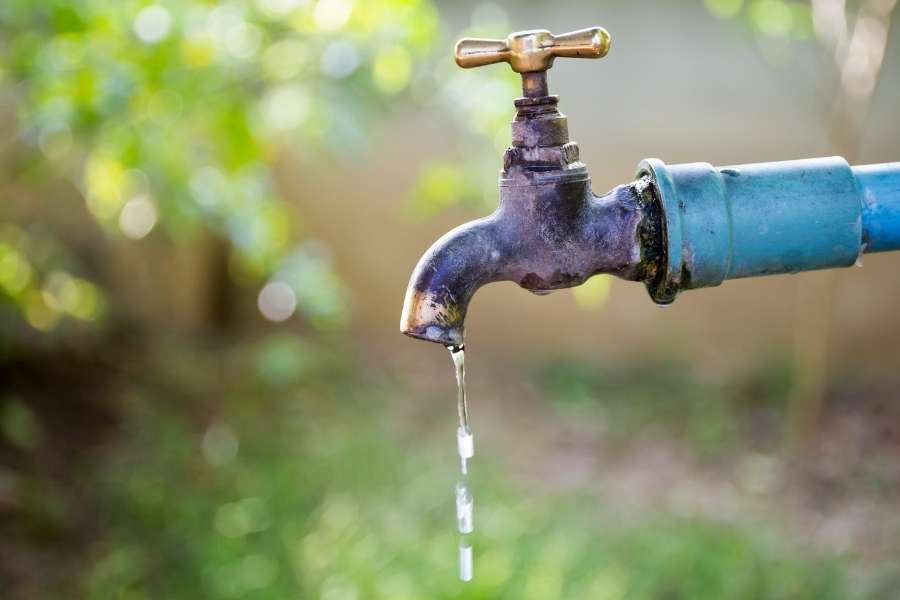 Un vieux robinet de jardin rouillé et usé laisse échapper des gouttes d'eau.