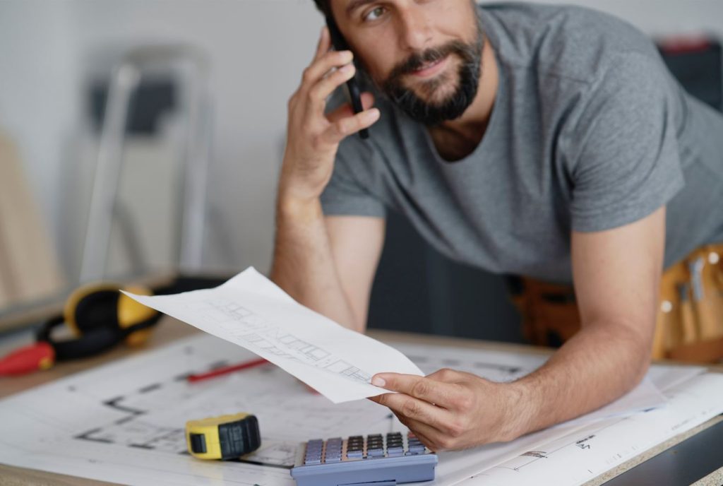 Un professionnel analyse un devis et des plans tout en téléphonant pour organiser des travaux au Maroc