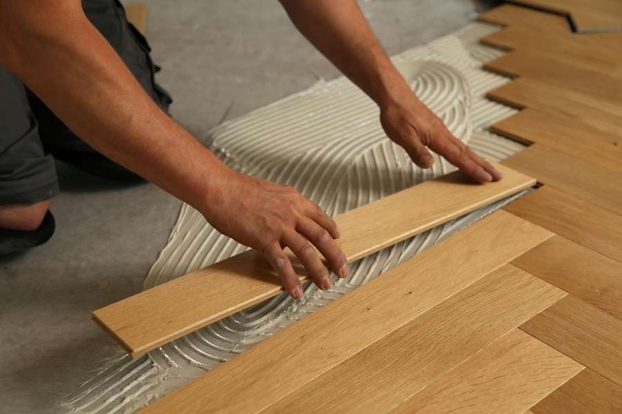Un artisan pose des lames de parquet flottant en bois clair sur une couche de colle peignée.